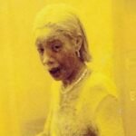 Realistic representation of a woman in professional attire covered in grey dust and ash in a New York lobby.