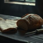 A loaf of colonial-era rye bread on a wooden table with a quill and parchment, representing the ergot theory of the Salem witch trials.