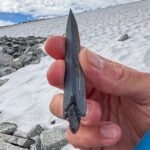 A prehistoric slate arrowhead and wooden shaft emerging from melting ice in the Norwegian mountains.