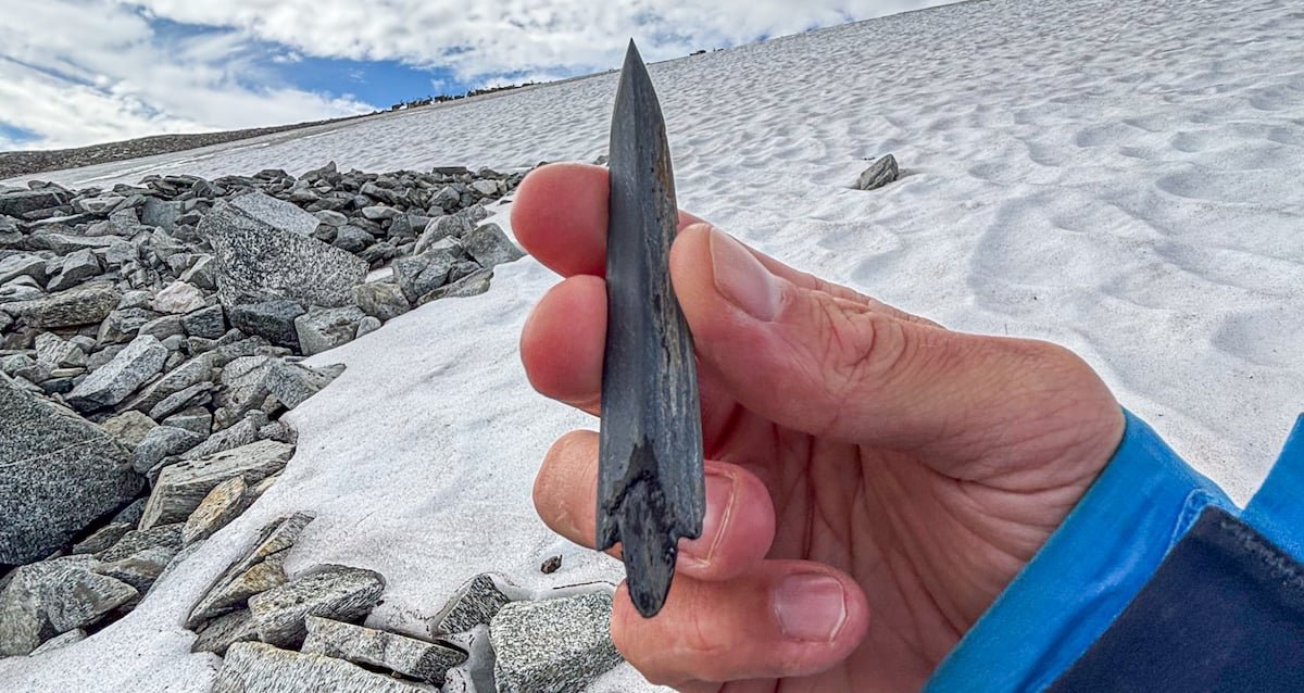 A prehistoric slate arrowhead and wooden shaft emerging from melting ice in the Norwegian mountains.